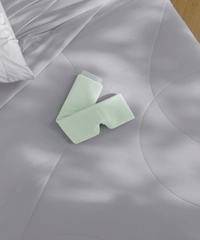 Breescape dual-sided cooling eye mask, mint green BlendTek™ fabric, on misty grey bedding.