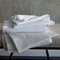 Two flat sheets in classic colors white and ivory folded on a bench.