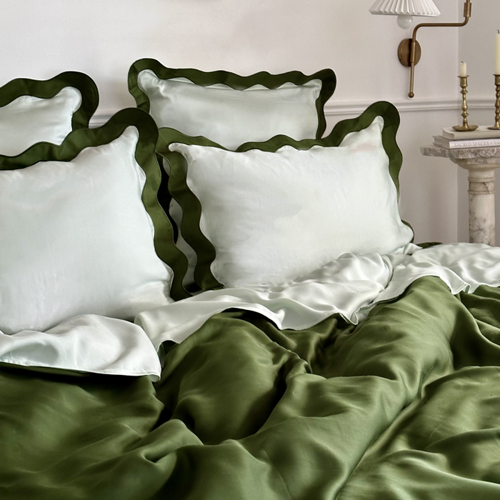 Eucalyptus bedding styled on a bed with scalloped edge pillowcases and smooth fabric in dark green and light green.