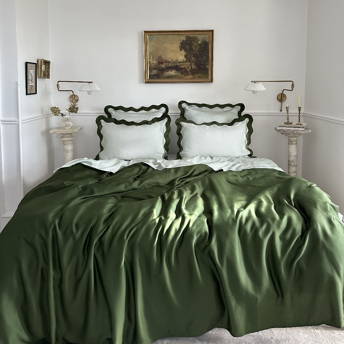Bedroom with eucalyptus tencel  bedding in with dark green and light green scalloped pillows, framed artwork on the wall.