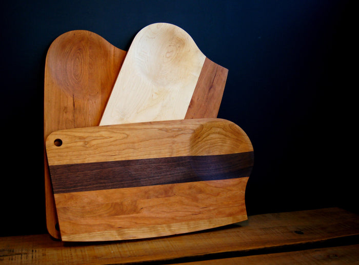 The TY Fine Furniture Mixed Wood Cutting Board with Integrated Bowl Serving Tray Large showcases its unique handmade charm, featuring varied shapes, sizes, and wood tones set against a dark background on a rustic wooden surface.