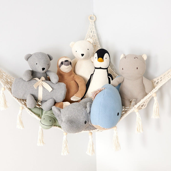 Collection of soft toys including bears, a penguin, and a sloth in a hammock against a white wall.