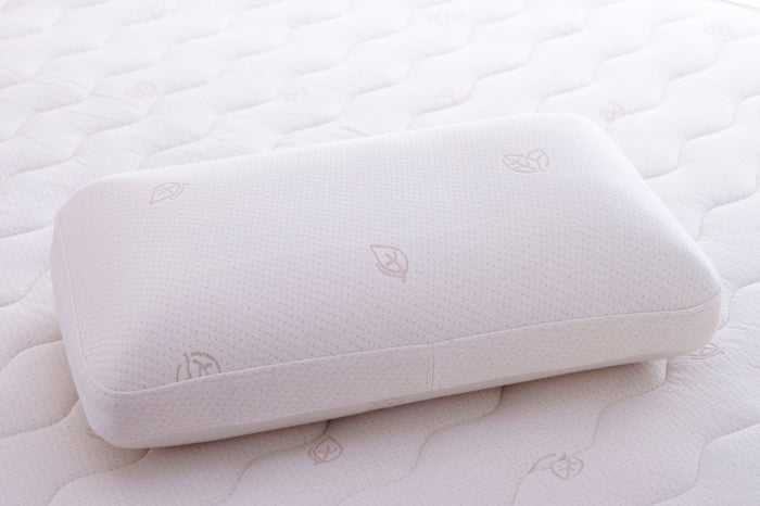 The Oxygen Pillow - Natural Fill by TY Sleep, in crisp white with a delicate leaf pattern, rests on a matching wavy quilted mattress—creating a clean, soft, minimalistic scene ideal for side sleepers seeking comfort and support.