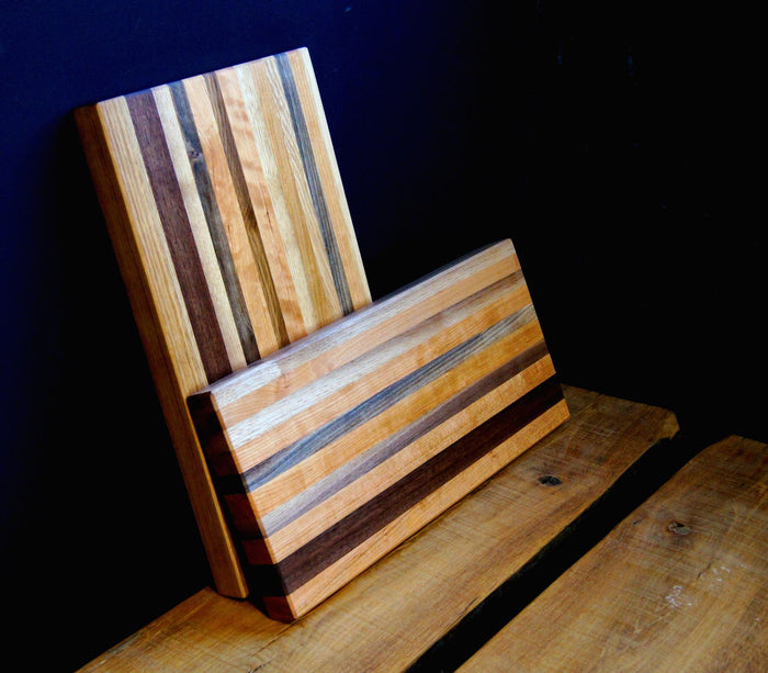 Two Solid Wood Butcher Block Cutting Boards by TY Fine Furniture, featuring alternating light and dark stripes and a food grade wood finish, are displayed on a wooden surface against a dark background.