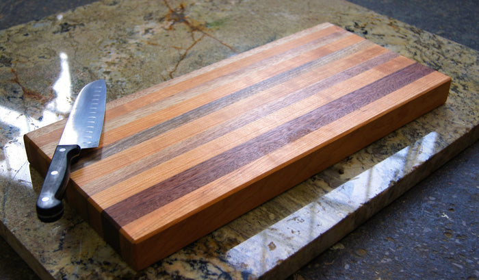 The TY Fine Furniture Solid Wood Butcher Block Cutting Board and a black-handled knife sit on a marbled countertop, highlighting the board's durable food-grade wood finish built for heavy use.