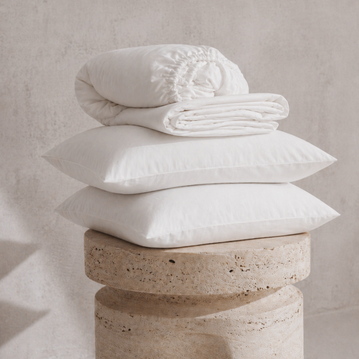 Stack of white pillows and a folded white blanket on a stone pedestal against a neutral background